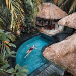 A woman enjoying leisure time floating in a tropical resort pool surrounded by lush greenery.